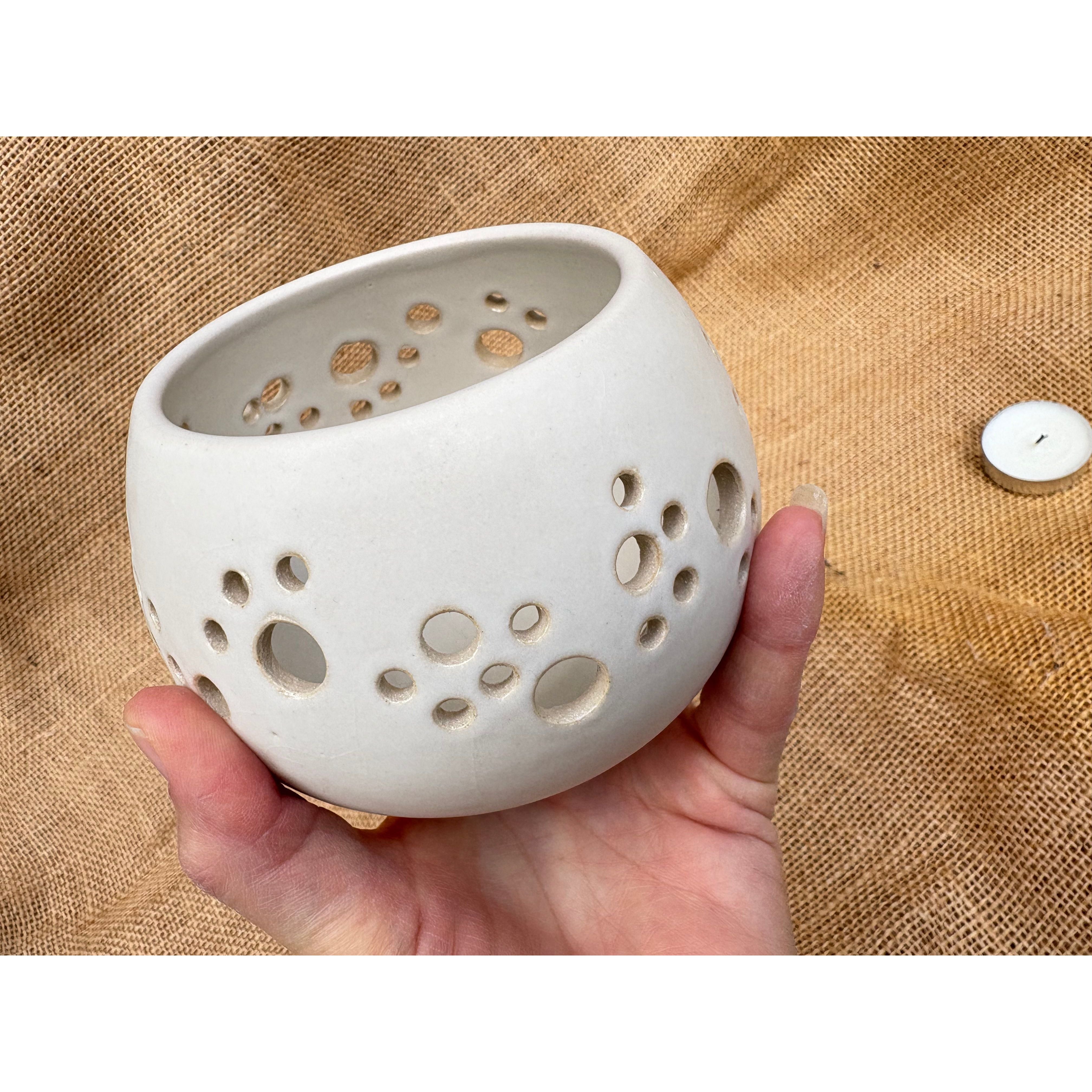 White ceramic holder with holes held in a hand against a textured beige background
